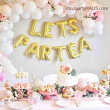 LETS PAR TEA Letter Balloons on back drop under a white and pink balloon garland and above a birthday cake table by partyHAUS