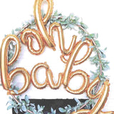 Oh baby balloons in gold script font in pretty gold ring wrapped in green floral leaves