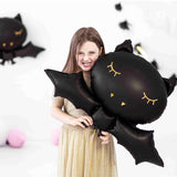 Girl holding large black matte bat balloon with gold eyes and fangs