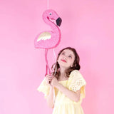 Girl holding pink flamingo pinata with gold wings